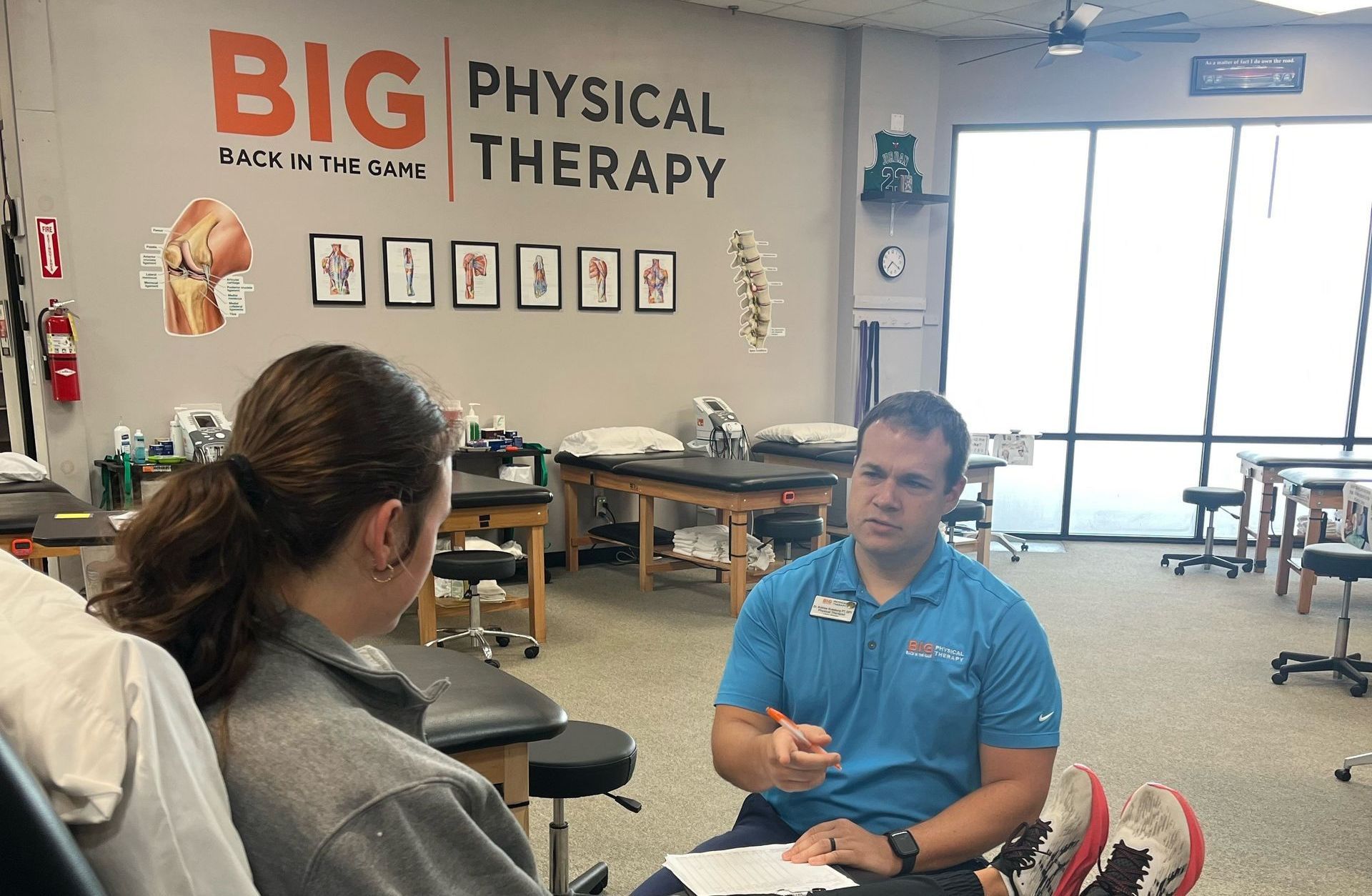 A man is talking to a woman in a physical therapy room.