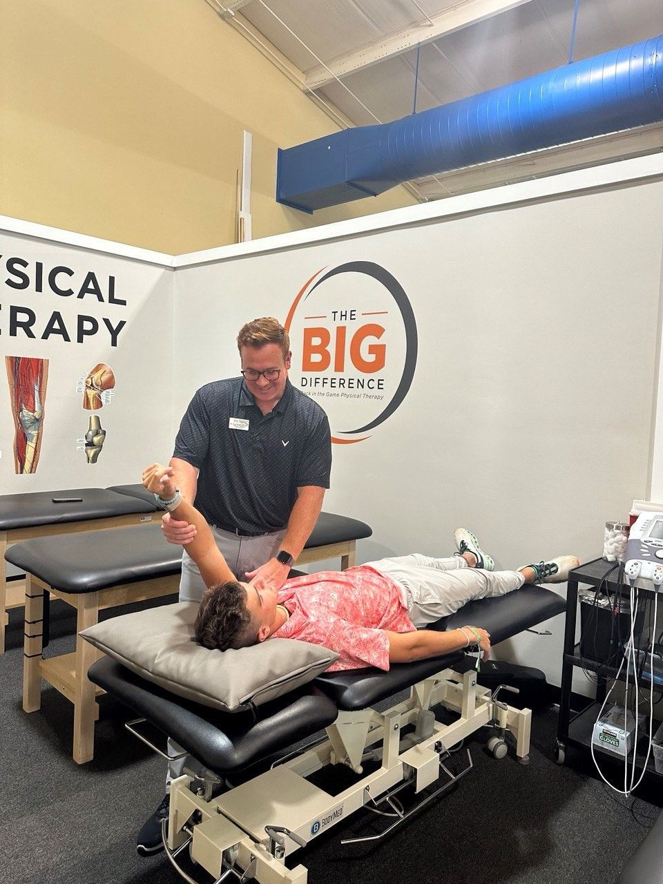 A man is stretching a woman 's arm on a table in a physical therapy room.