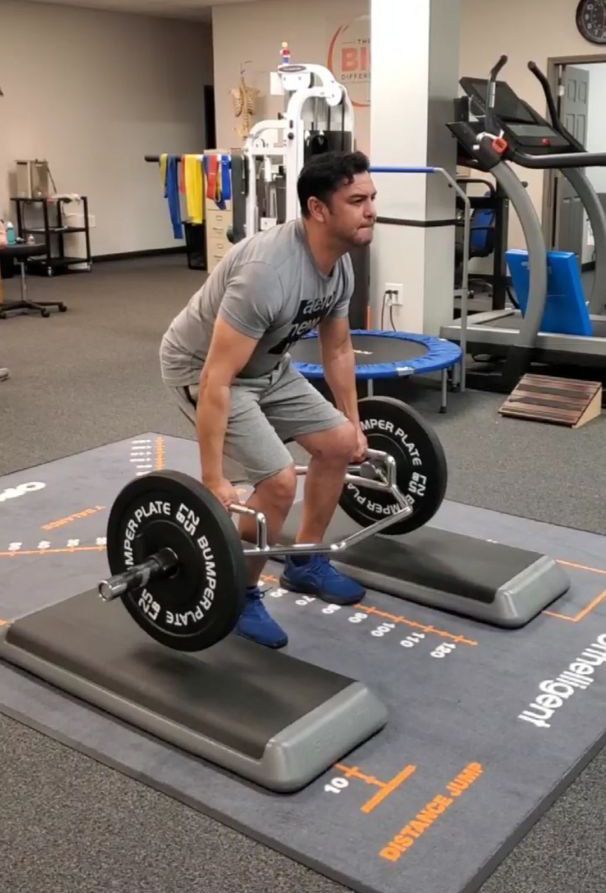 a man is lifting a barbell in a gym - using strength training to benefit his physical therapy 