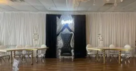 A throne and tables set up for an event in a hall with black and white draping.