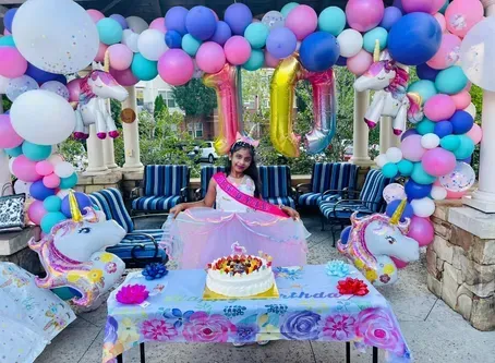 Girl's 10th birthday celebration. Balloons, unicorn decorations. Girl in pink dress, cake. Outdoor setting.