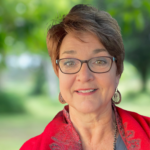 Woman with short brown hair, glasses, and red jacket smiles outdoors.