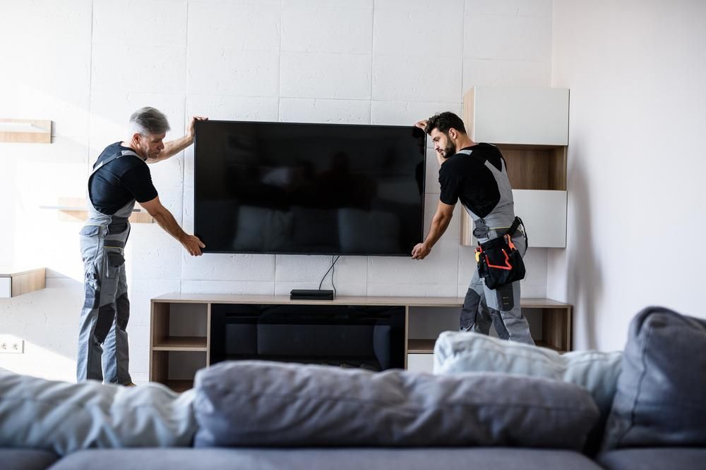 Two Men Are Installing A Flat Screen Tv In A Living Room — Highfields Antennas In Blackbutt, QLD