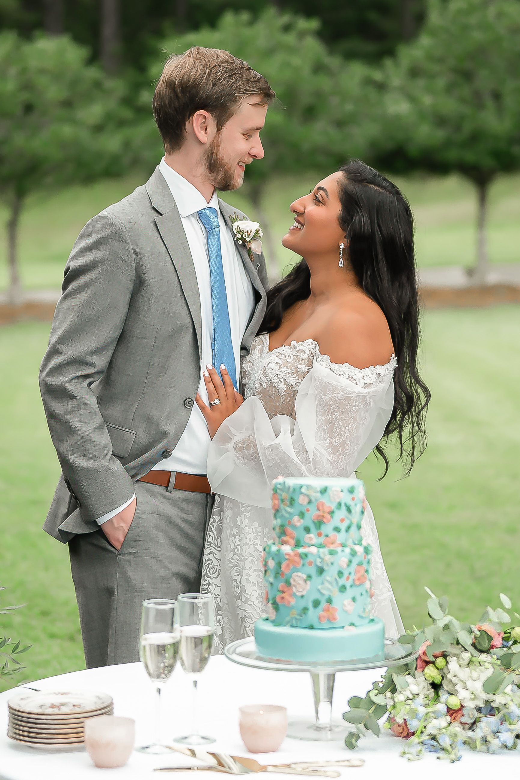 A bride and groom are standing next to a cake on a table.