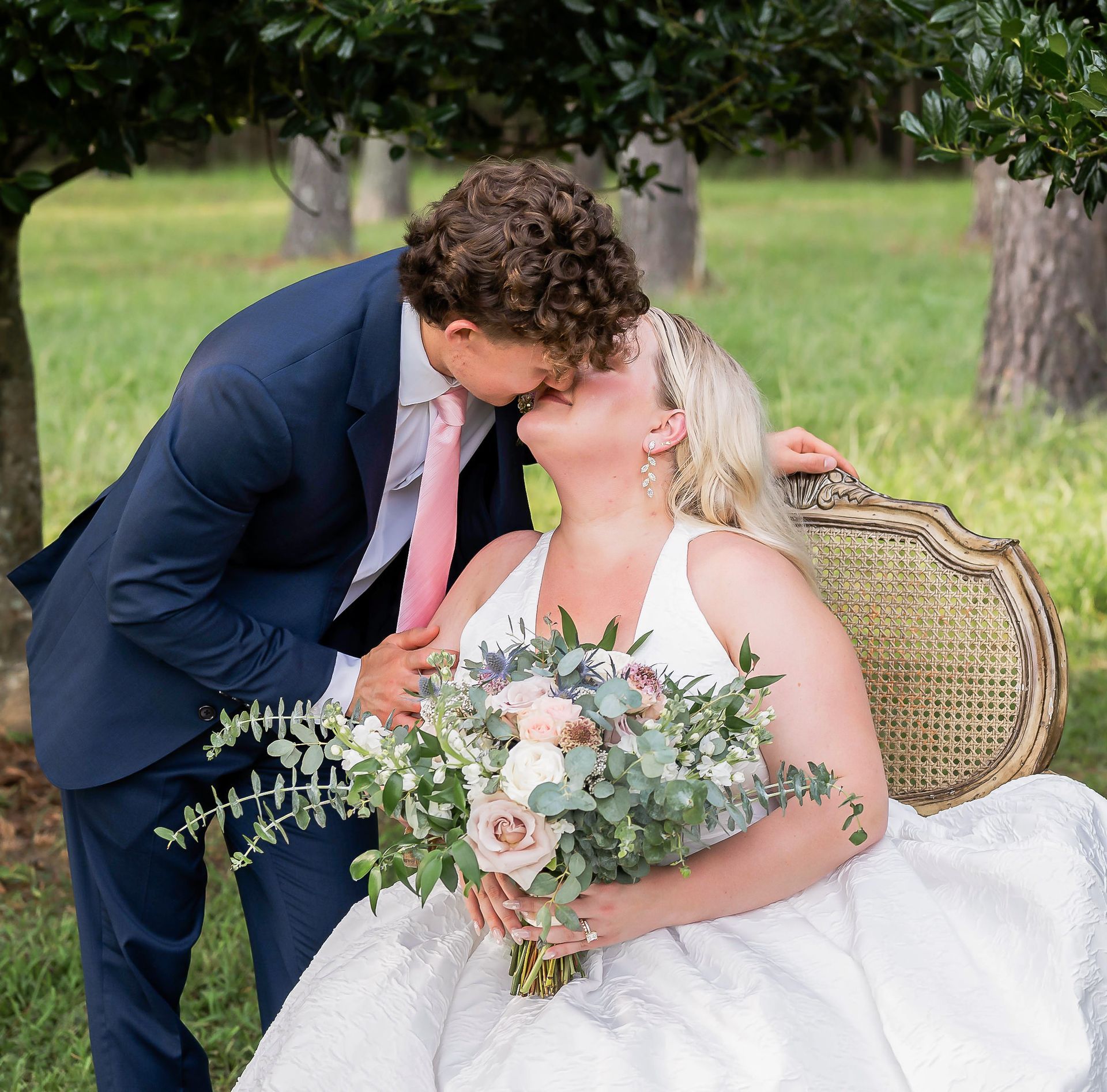 A man in a suit and tie is kissing a woman in a white dress holding a bouquet of flowers.