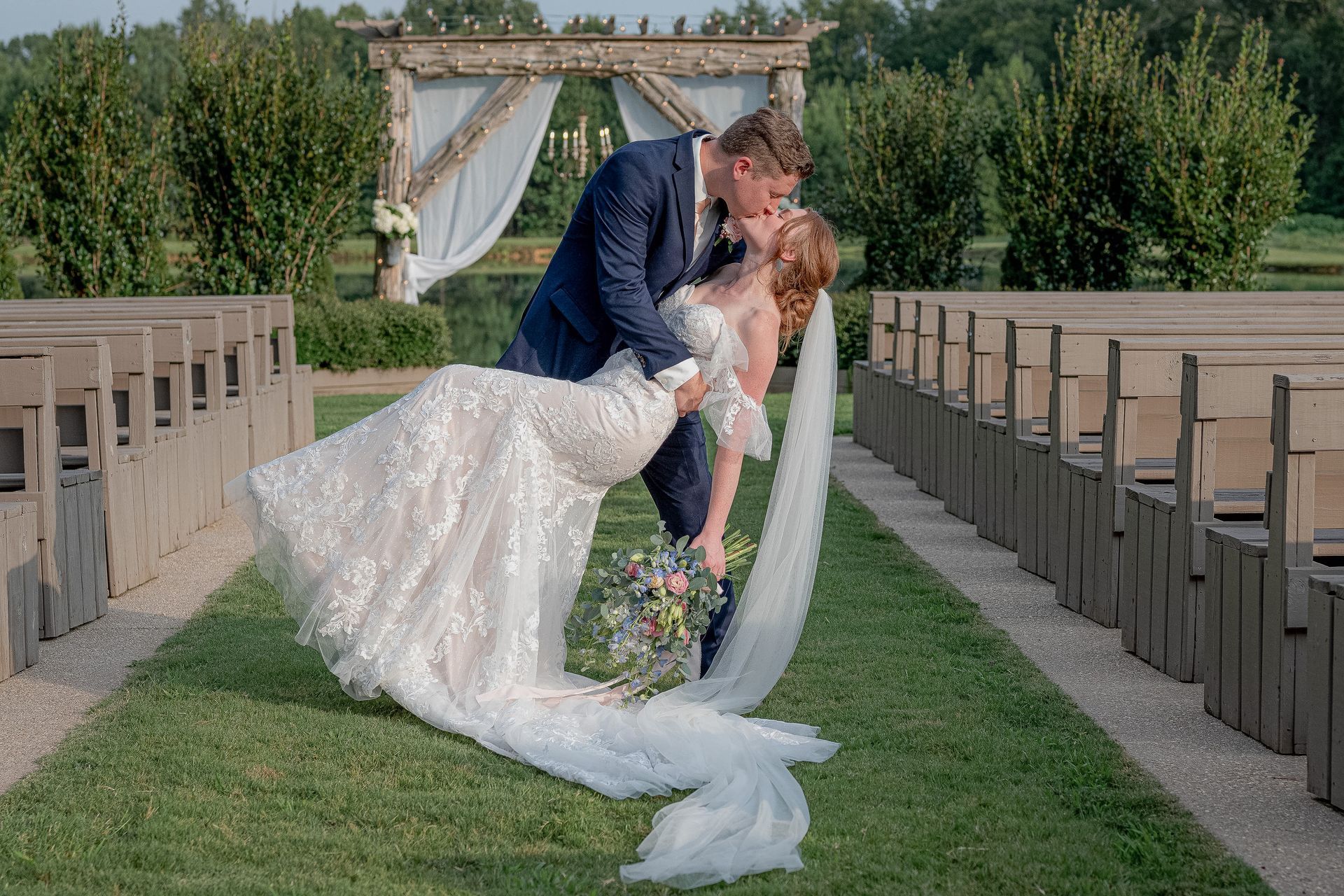 A bride and groom are kissing on the aisle of a church.