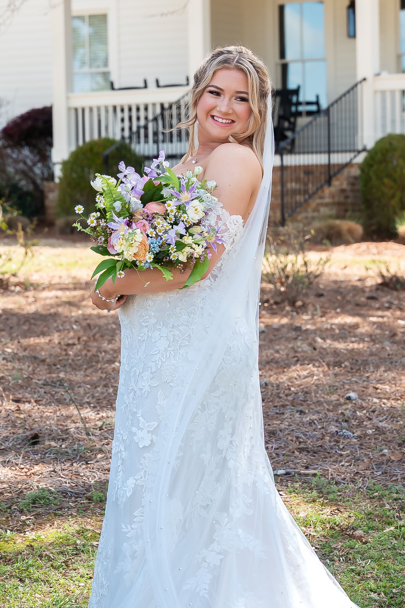 A bride in a wedding dress is holding a bouquet of flowers in front of a house.