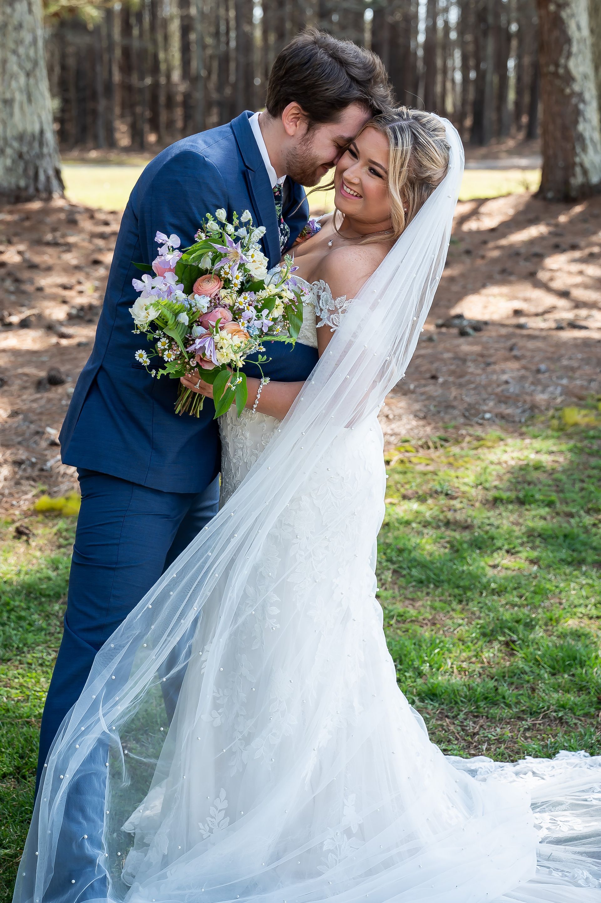 A bride and groom are kissing in the grass on their wedding day.