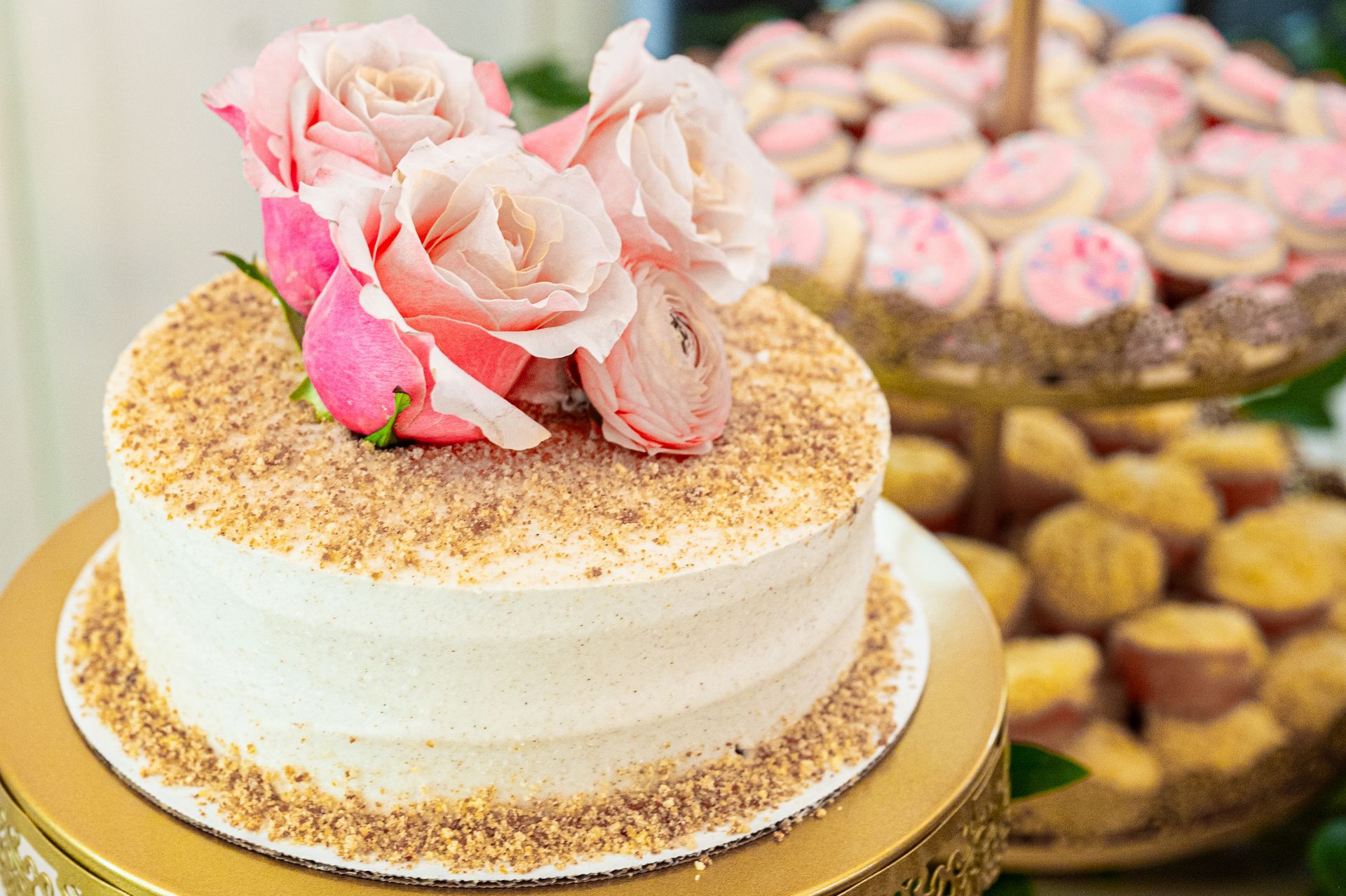 A white cake with pink roses on top is sitting on top of a gold cake stand.