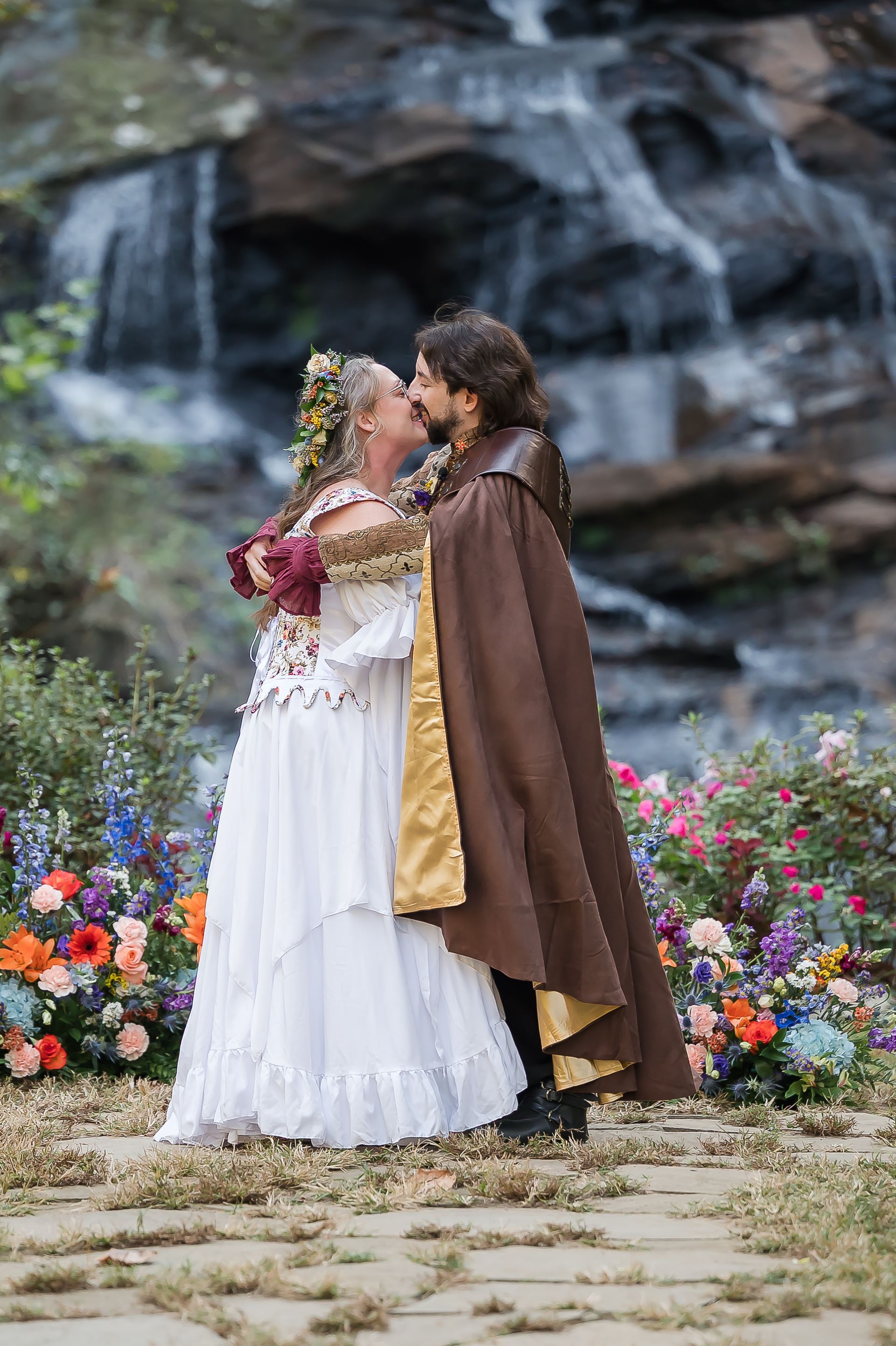 A bride and groom are kissing in front of a waterfall.