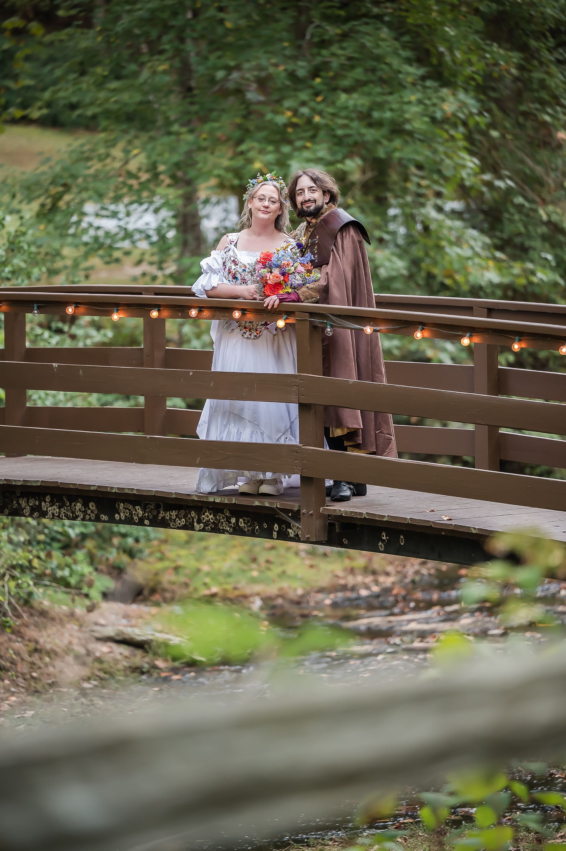 A bride and groom are posing for a picture on a wooden bridge.