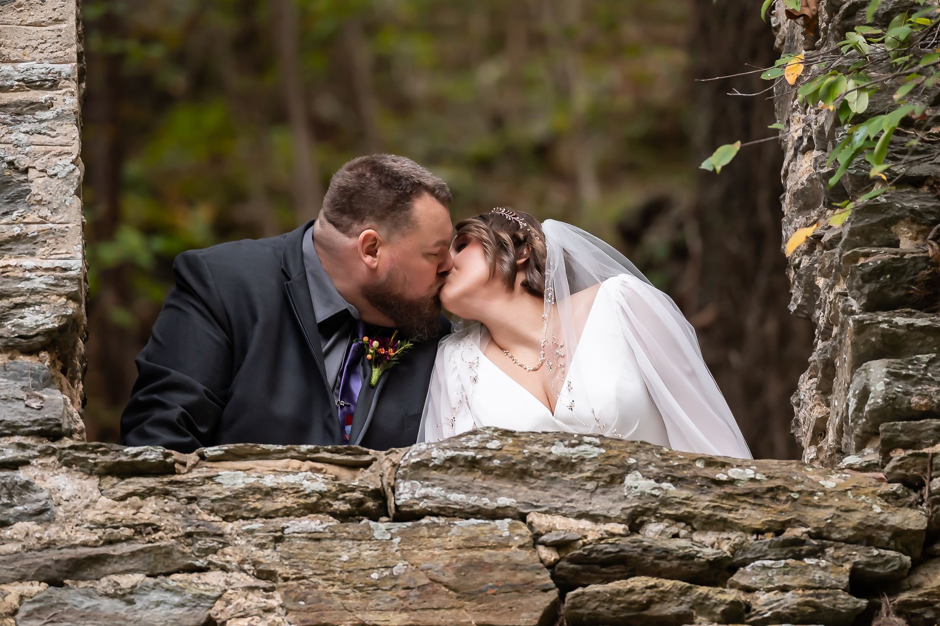 A bride and groom are kissing in front of a stone wall.