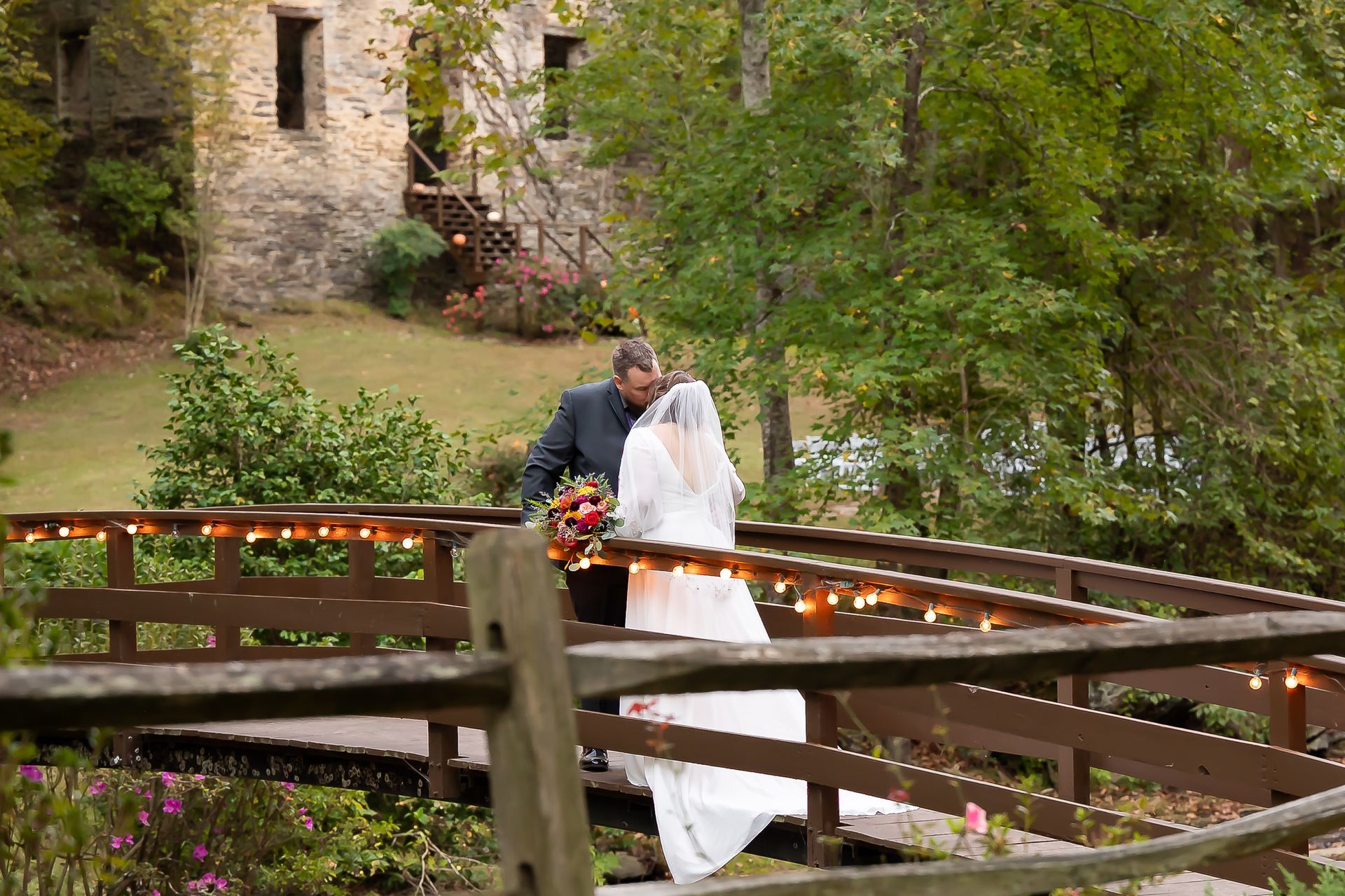 A bride and groom are kissing on a wooden bridge.