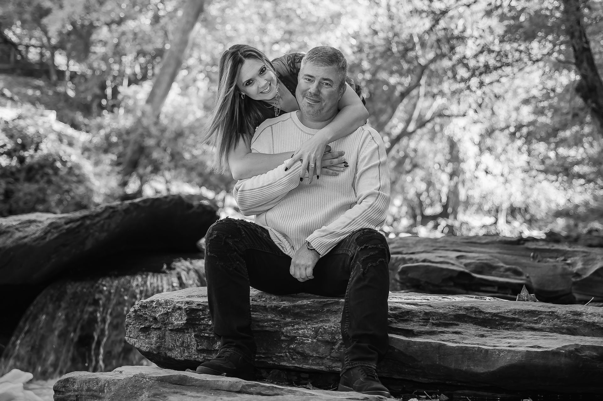 A man and a woman are sitting on a rock in the woods.