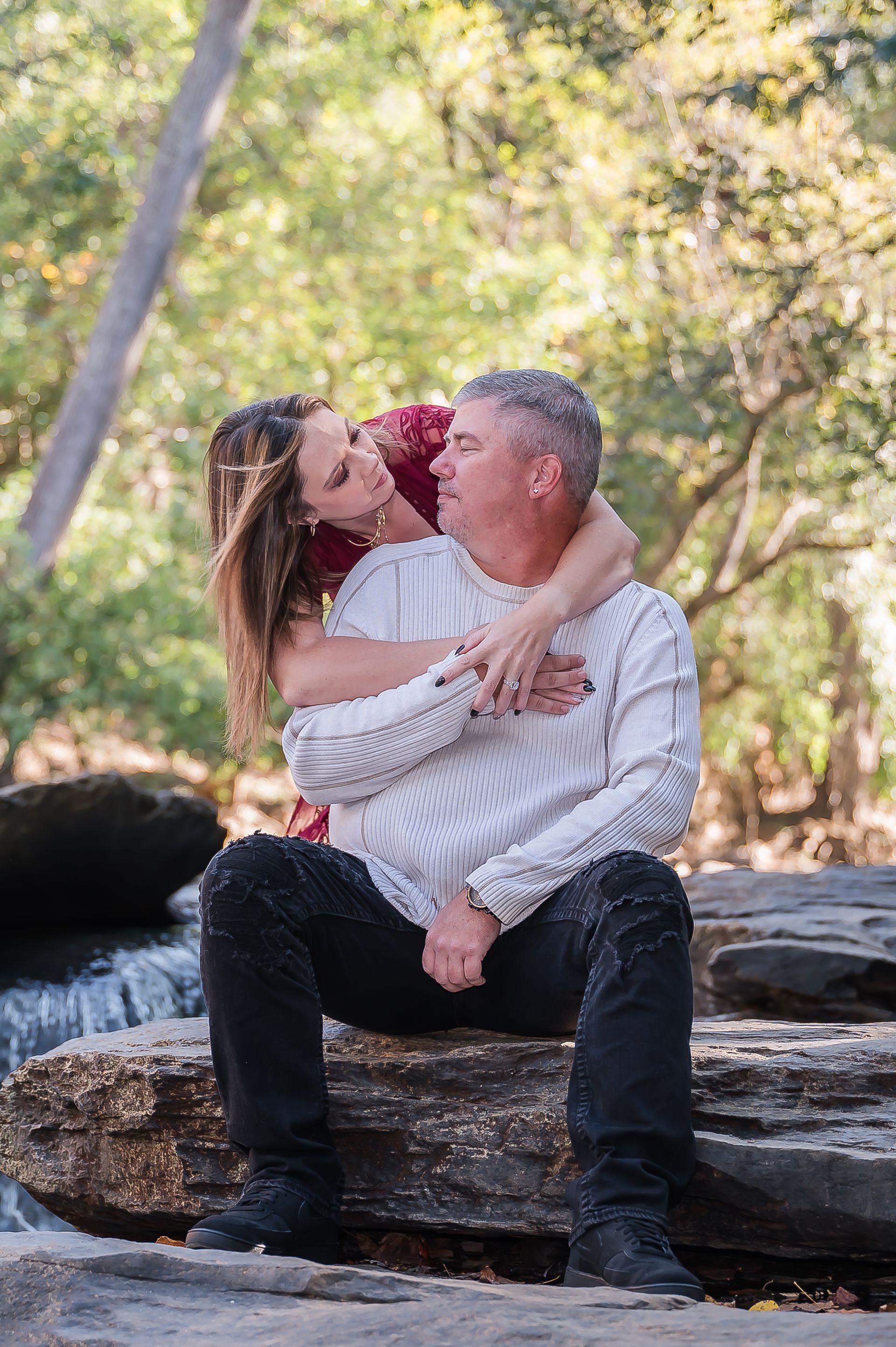 A man and a woman are sitting on a rock near a waterfall.