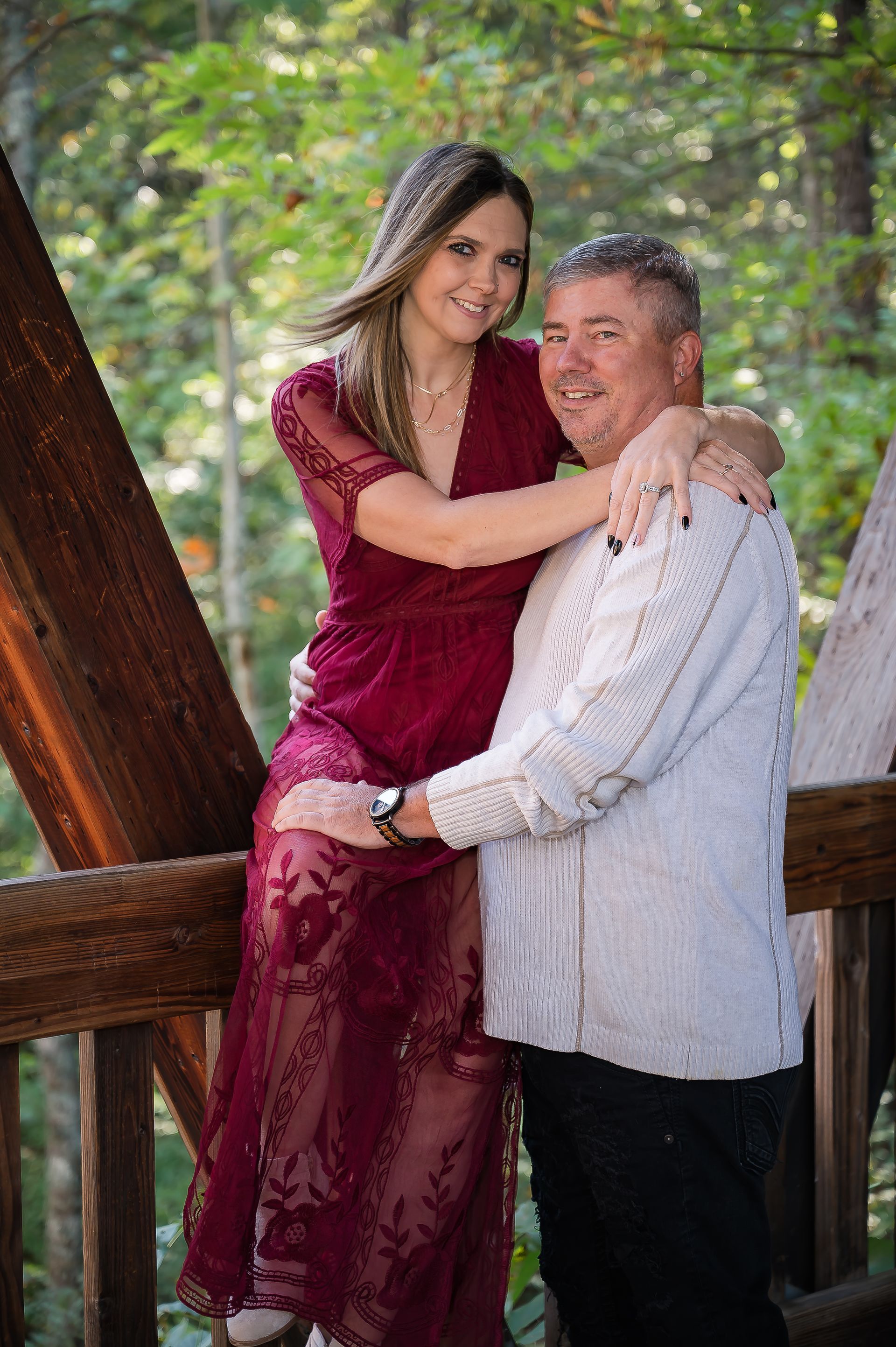 A man and a woman are posing for a picture on a bridge . the woman is wearing a red dress.