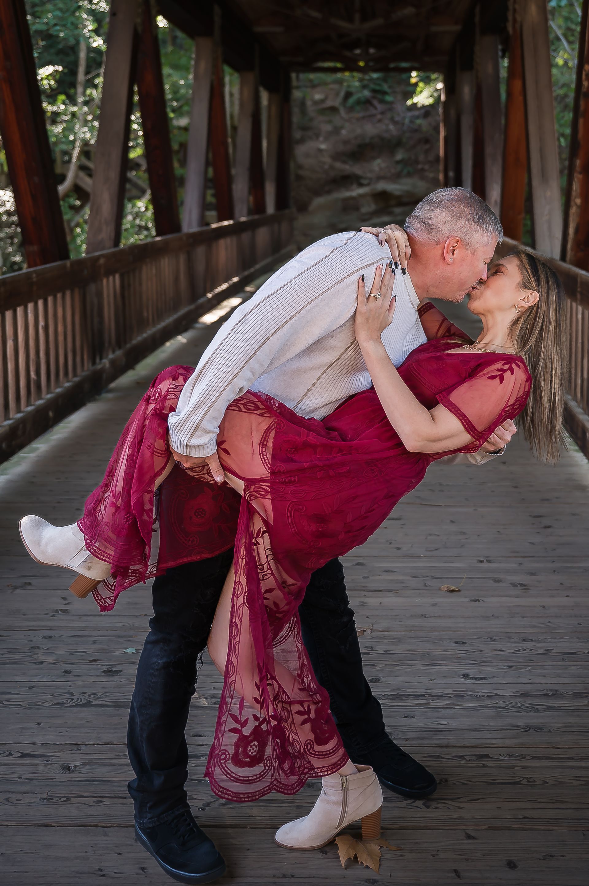 A man is holding a woman in his arms and kissing her on a bridge.