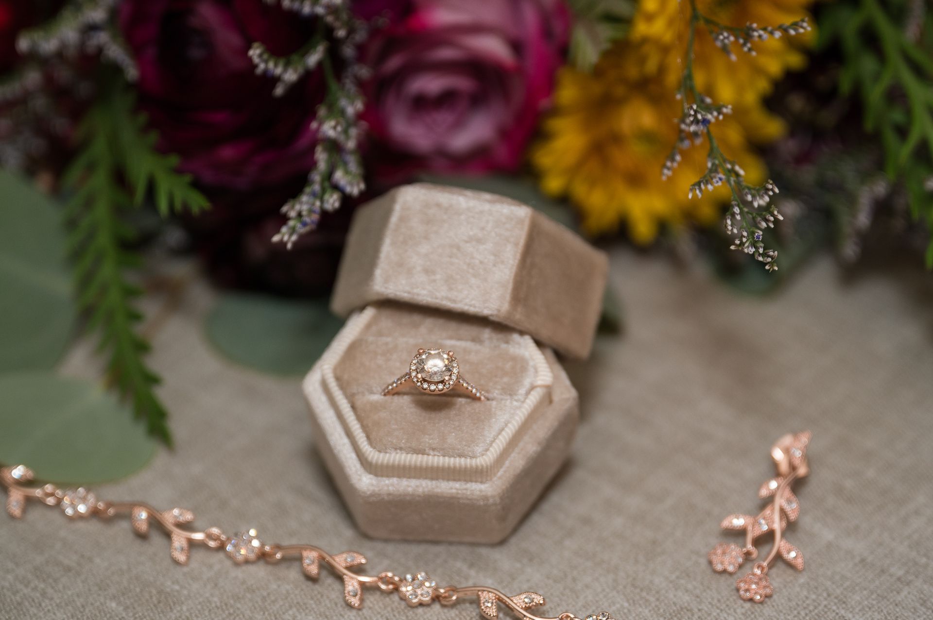 A wedding ring and bracelet are sitting on a table next to a bouquet of flowers.