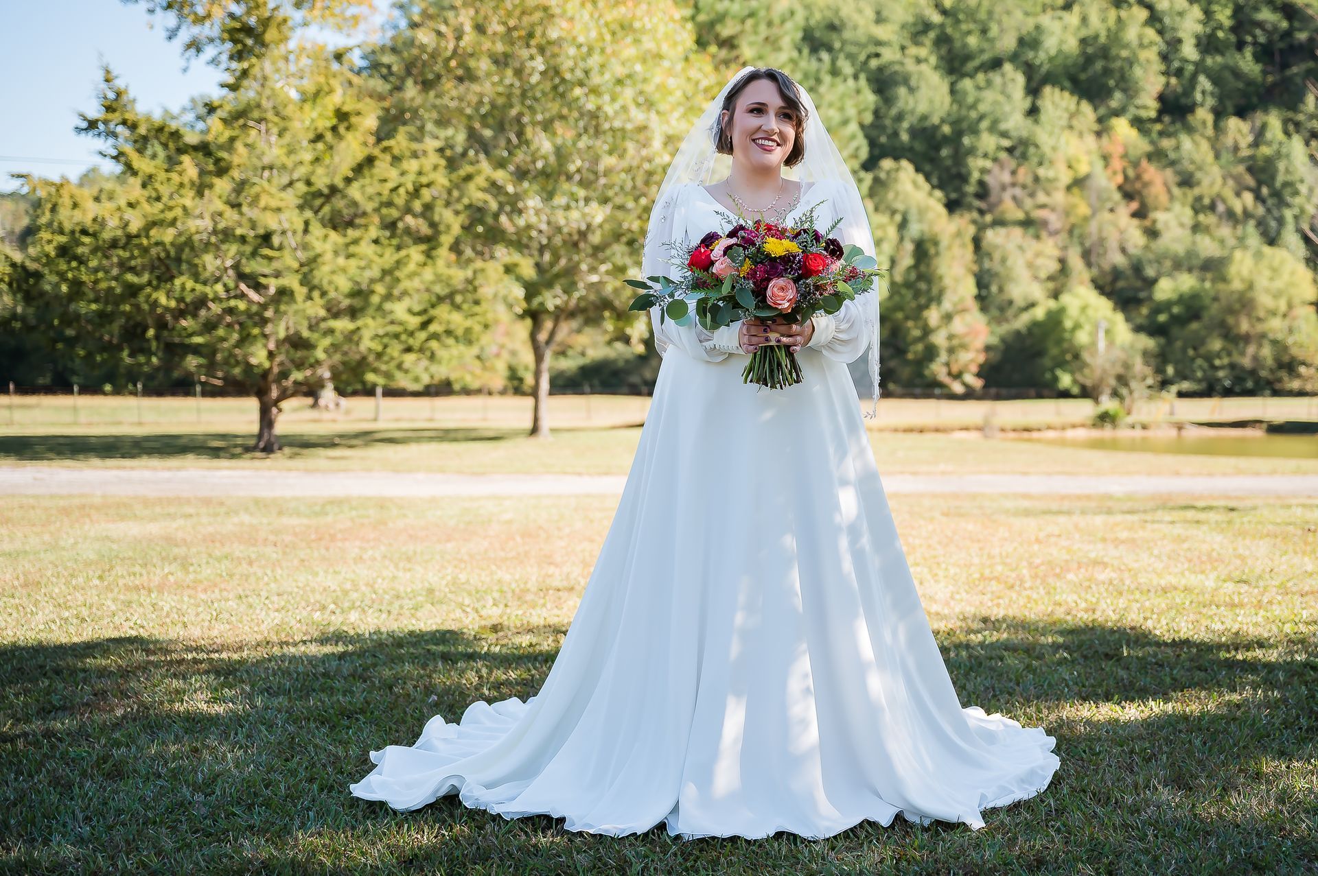 A bride in a wedding dress is standing in a field holding a bouquet of flowers.