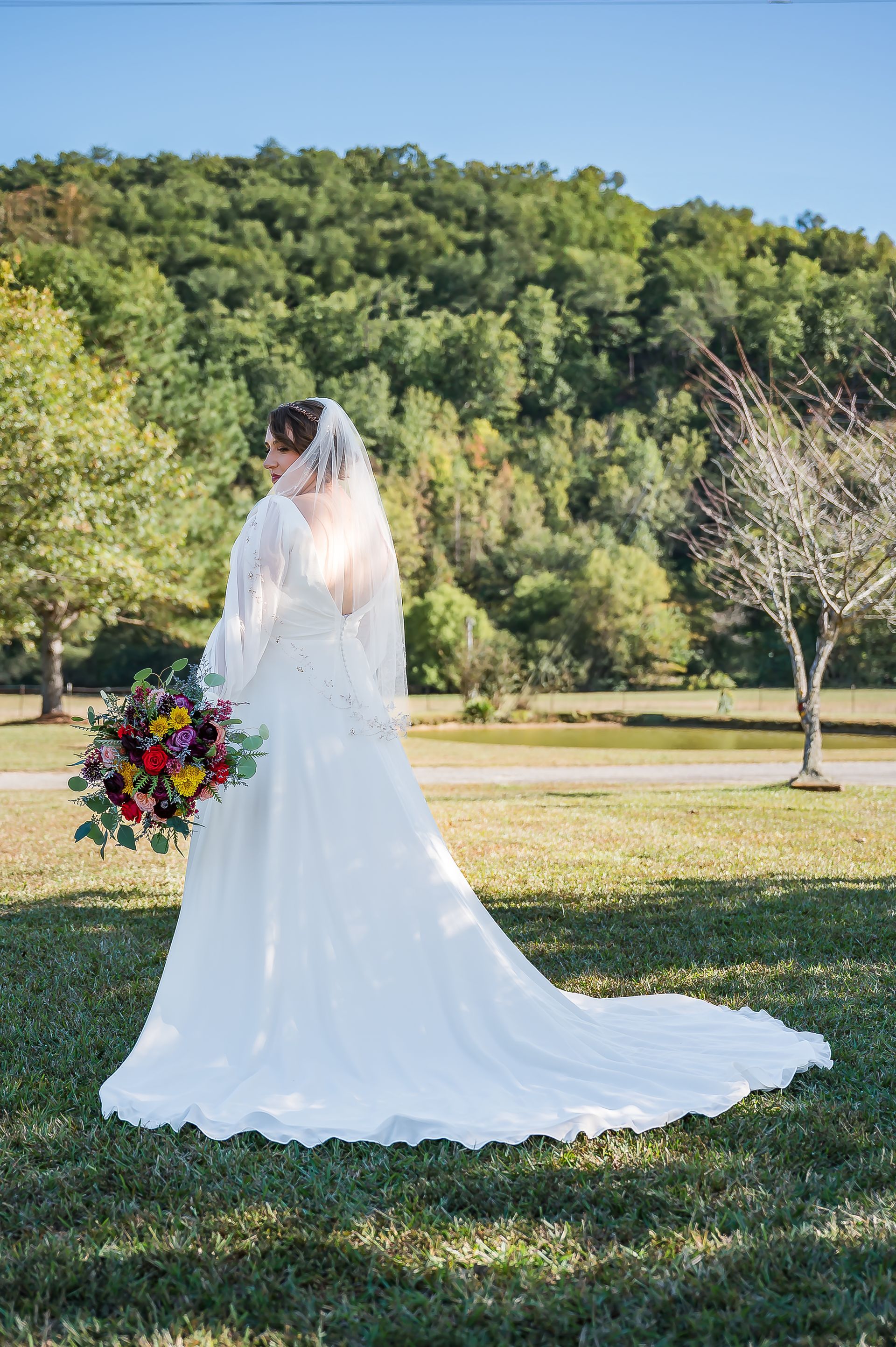 A bride in a wedding dress is standing in a field holding a bouquet of flowers.