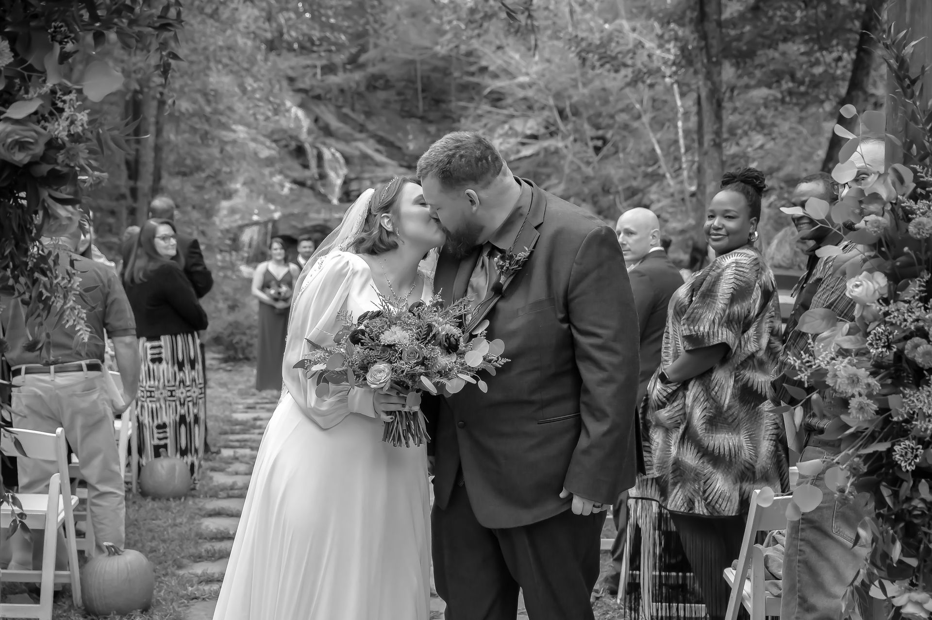 A black and white photo of a bride and groom kissing at their wedding ceremony.