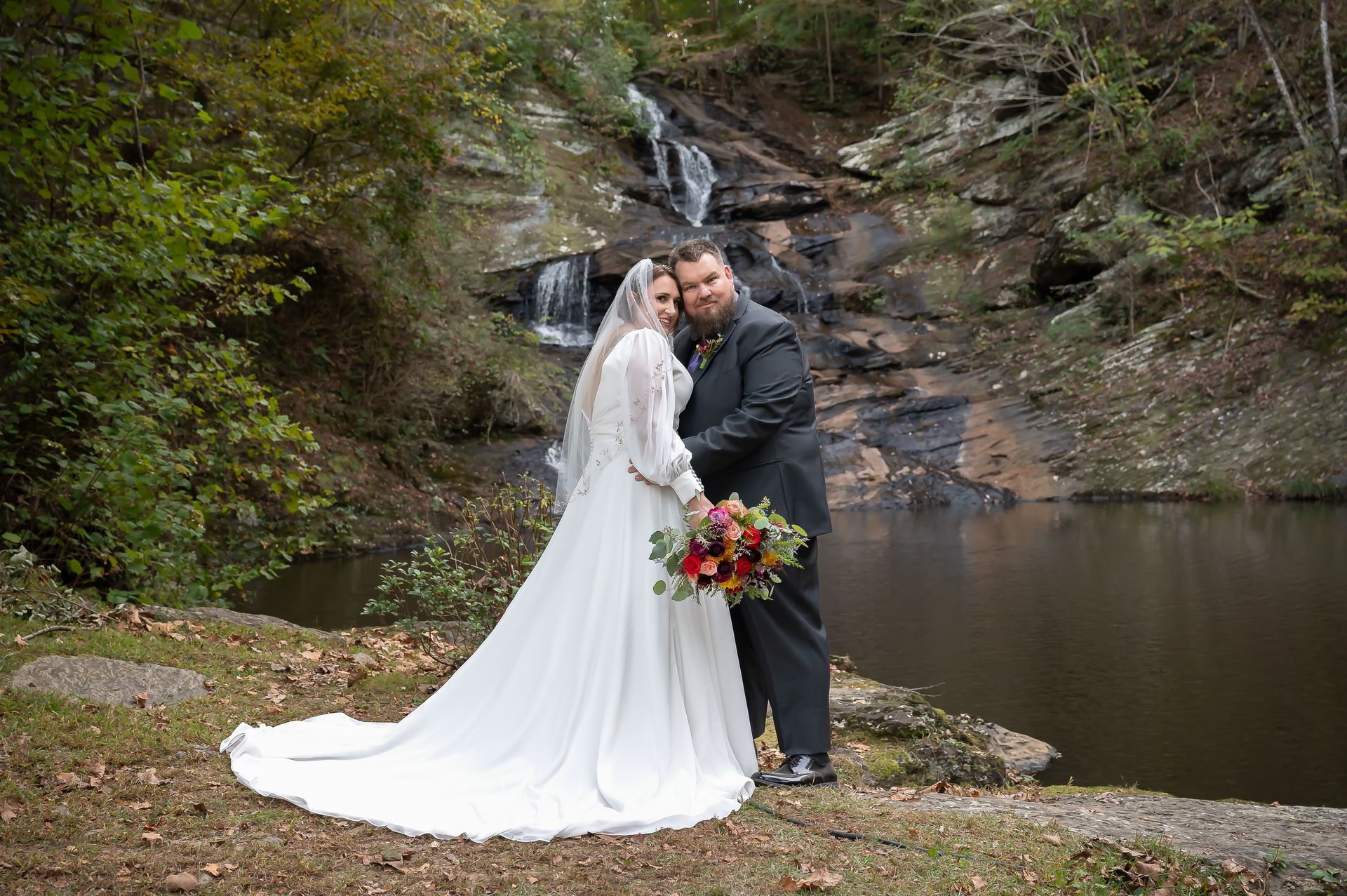 A bride and groom are posing for a picture in front of a waterfall.
