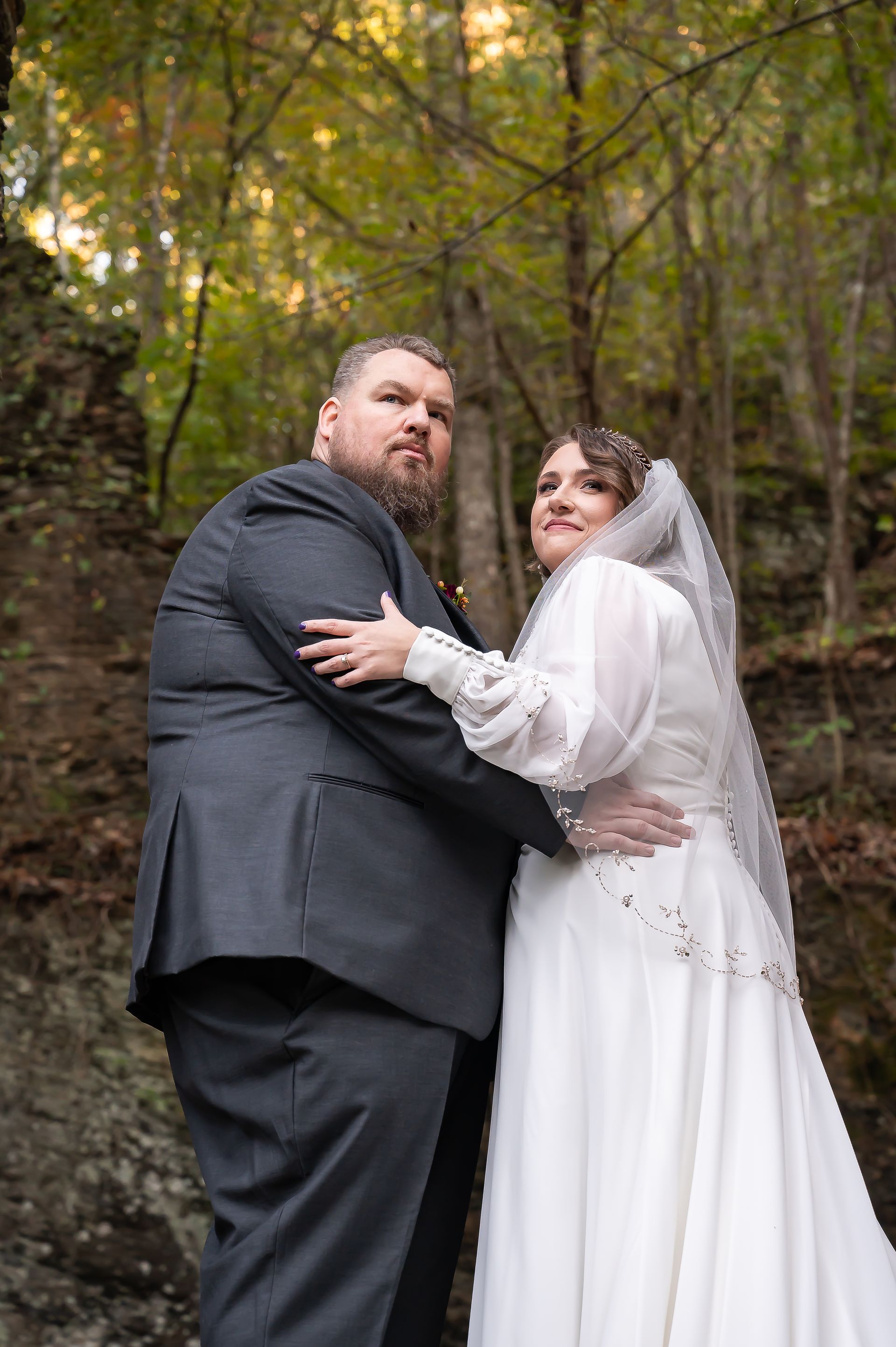 A bride and groom are posing for a picture in the woods.