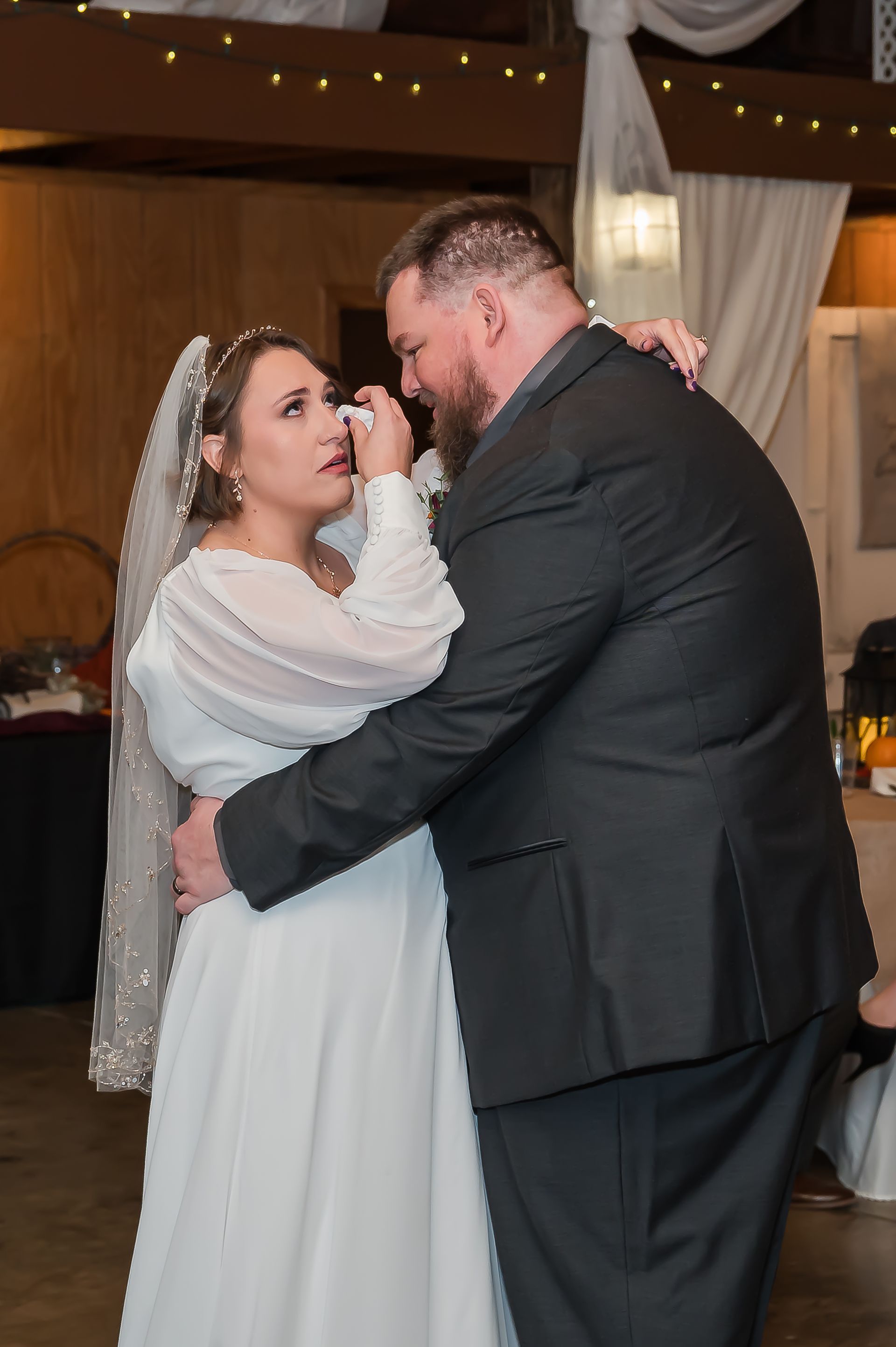 A bride and groom are dancing at their wedding reception and the bride is crying.