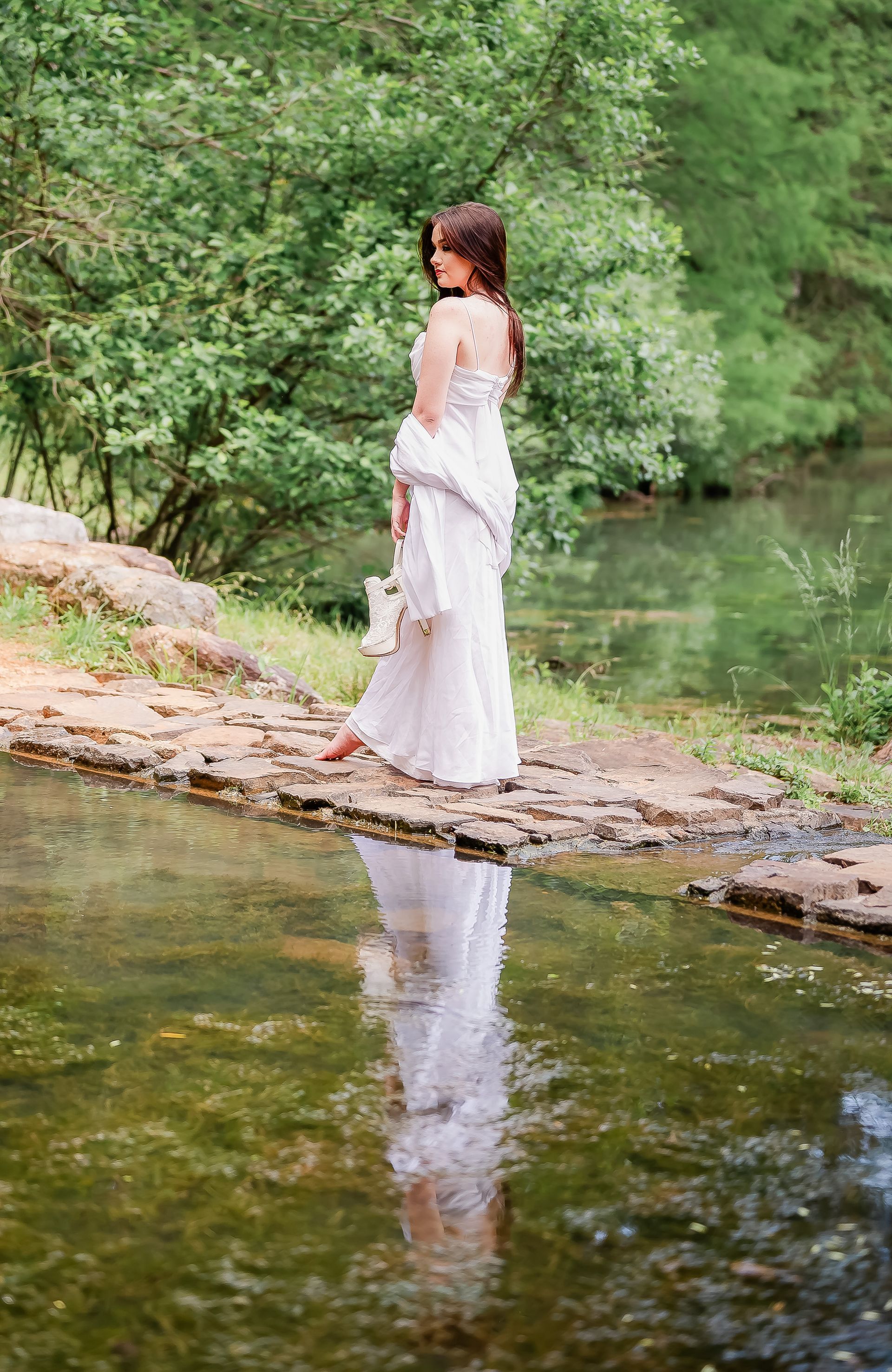 A woman in a white dress is standing on a stone bridge over a river.