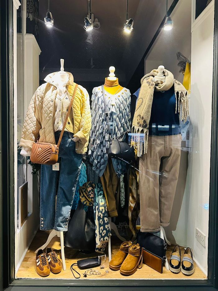 Mannequins in a boutique window display winter outfits, scarves, jeans, and boots.