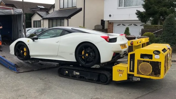 White sports car loaded on a yellow tow dolly in a residential driveway