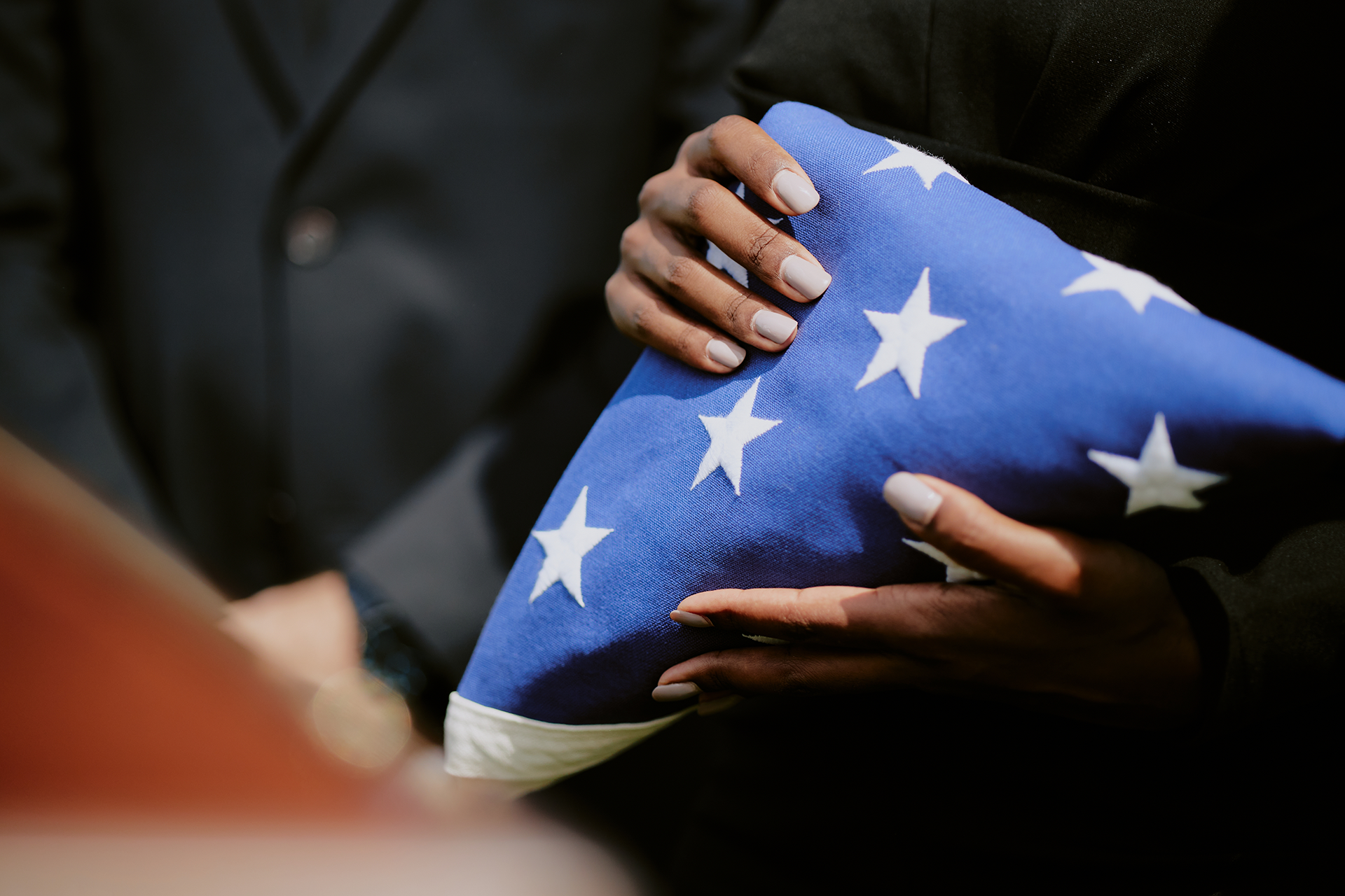 A woman is holding an american flag and a rose at a funeral.