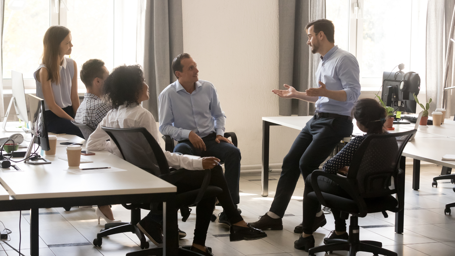 A group of people are sitting at tables in an office having a meeting.