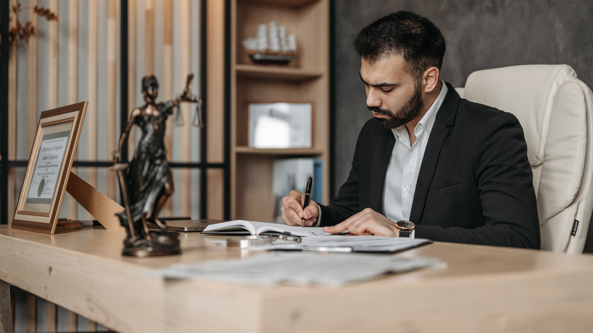 A man in a suit is sitting at a desk in front of a statue of justice.