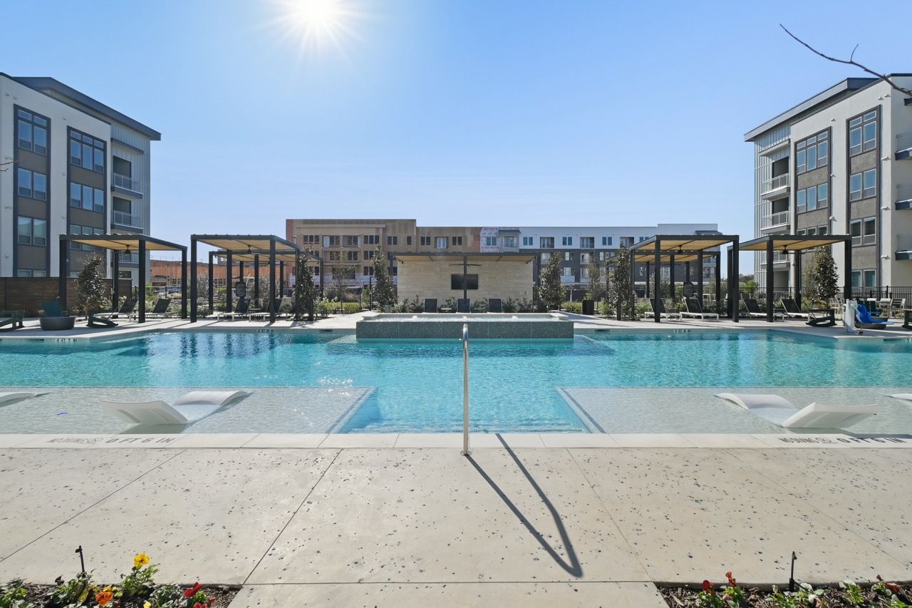 Outdoor apartment community pool with cabanas, lounge chairs, and modern buildings surrounding at Ennova Fulshear in Fulshear, TX.
