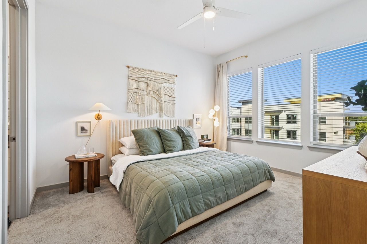 Bright bedroom with a queen bed, green quilt, two nightstands, and large windows  at Ennova Fulshear in Fulshear, TX.
