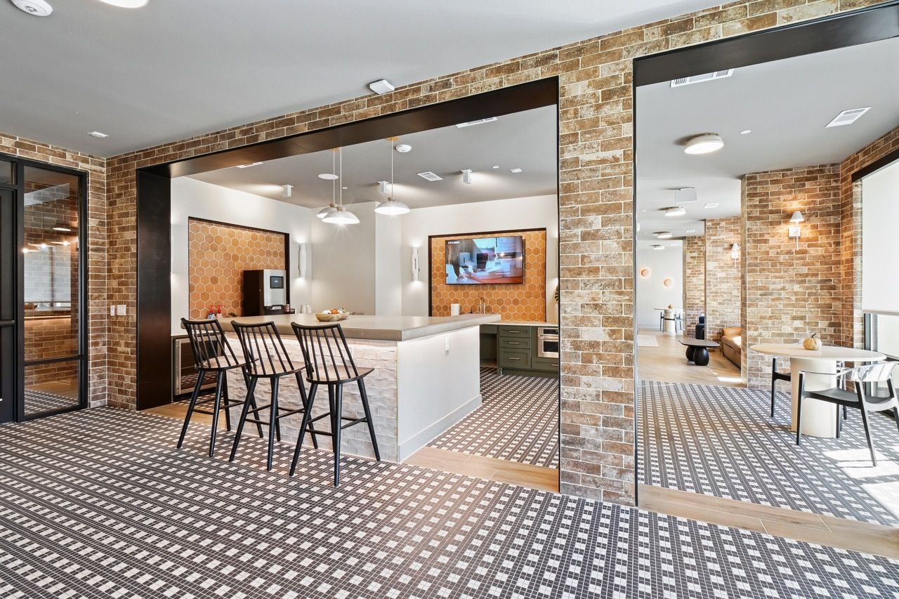 Interior community lounge with brick walls, a central bar, and seating at Ennova Fulshear in Fulshear, TX.