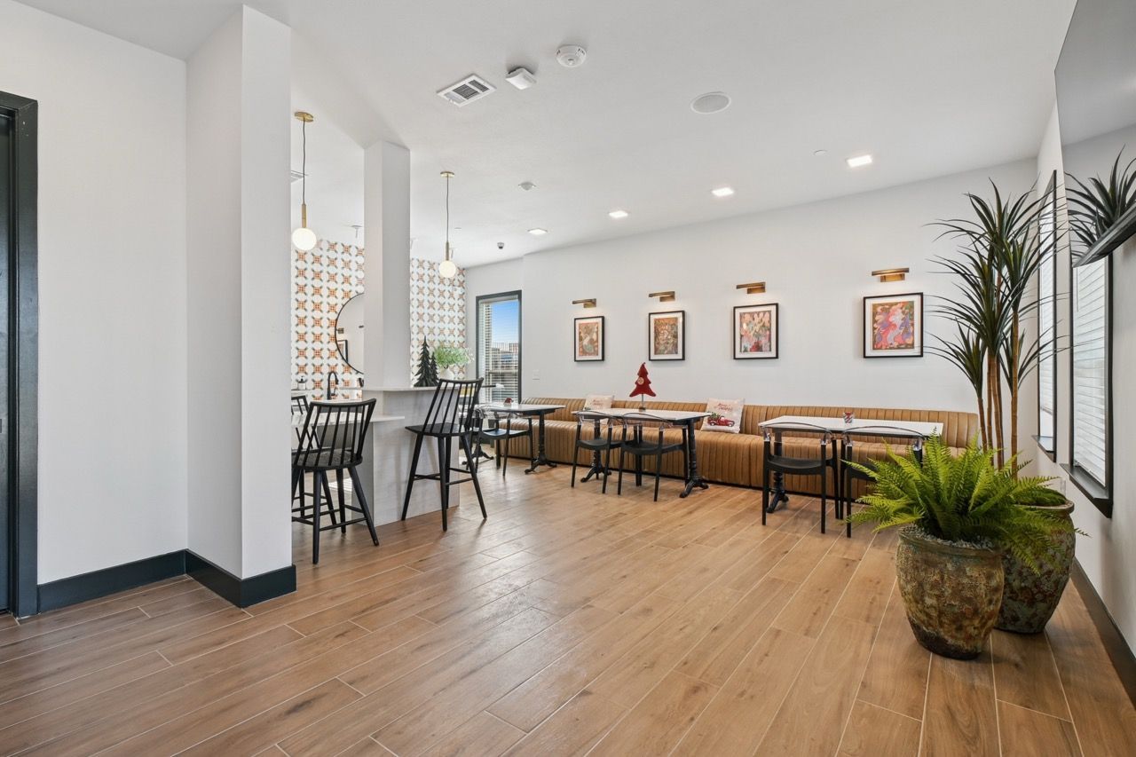Bright modern resident lounge with a bar counter, high chairs, tables, and large potted plants at Ennova Fulshear in Fulshear, TX.