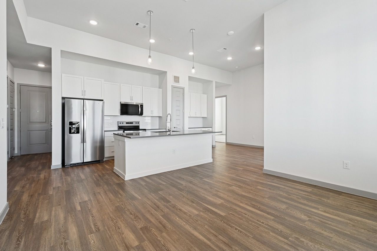 Open-concept kitchen with white cabinets, stainless steel appliances, and island  at Ennova Fulshear in Fulshear, TX.