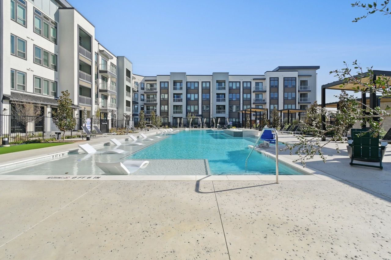Outdoor communal pool area in a modern apartment complex with lounge chairs at Ennova Fulshear in Fulshear, TX.