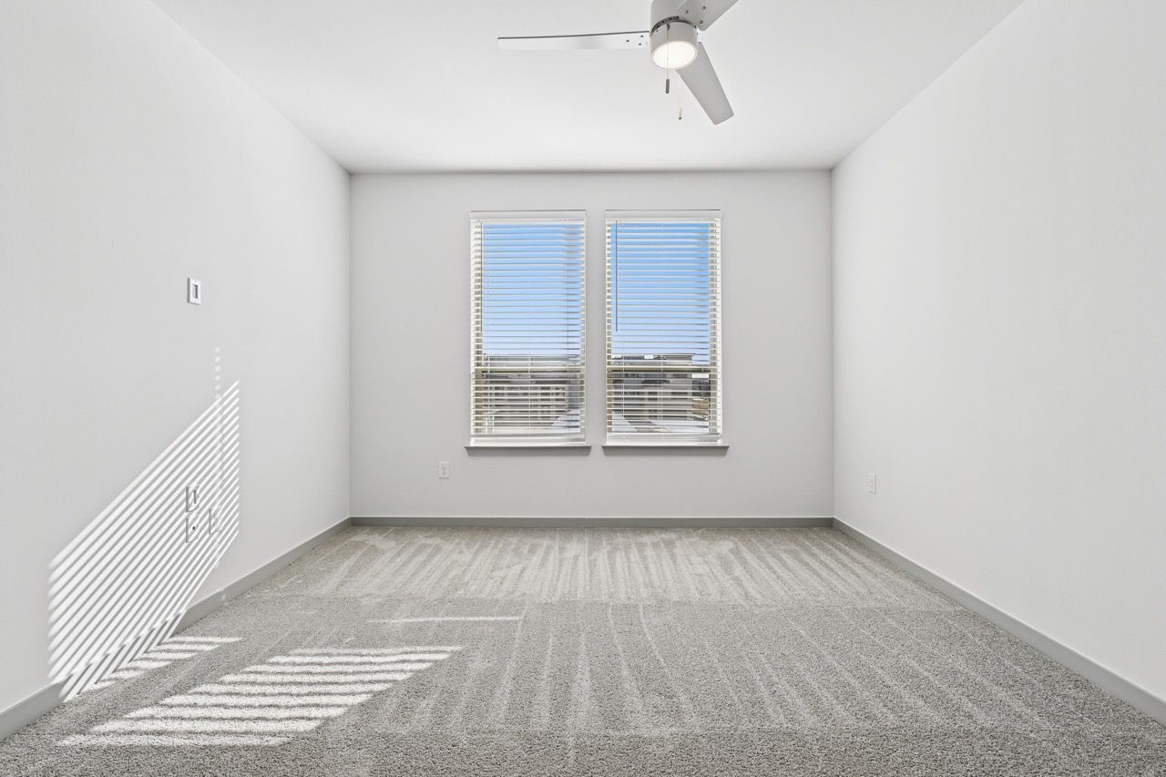 Empty white room with two windows, blinds, and a ceiling fan  at Ennova Fulshear in Fulshear, TX.