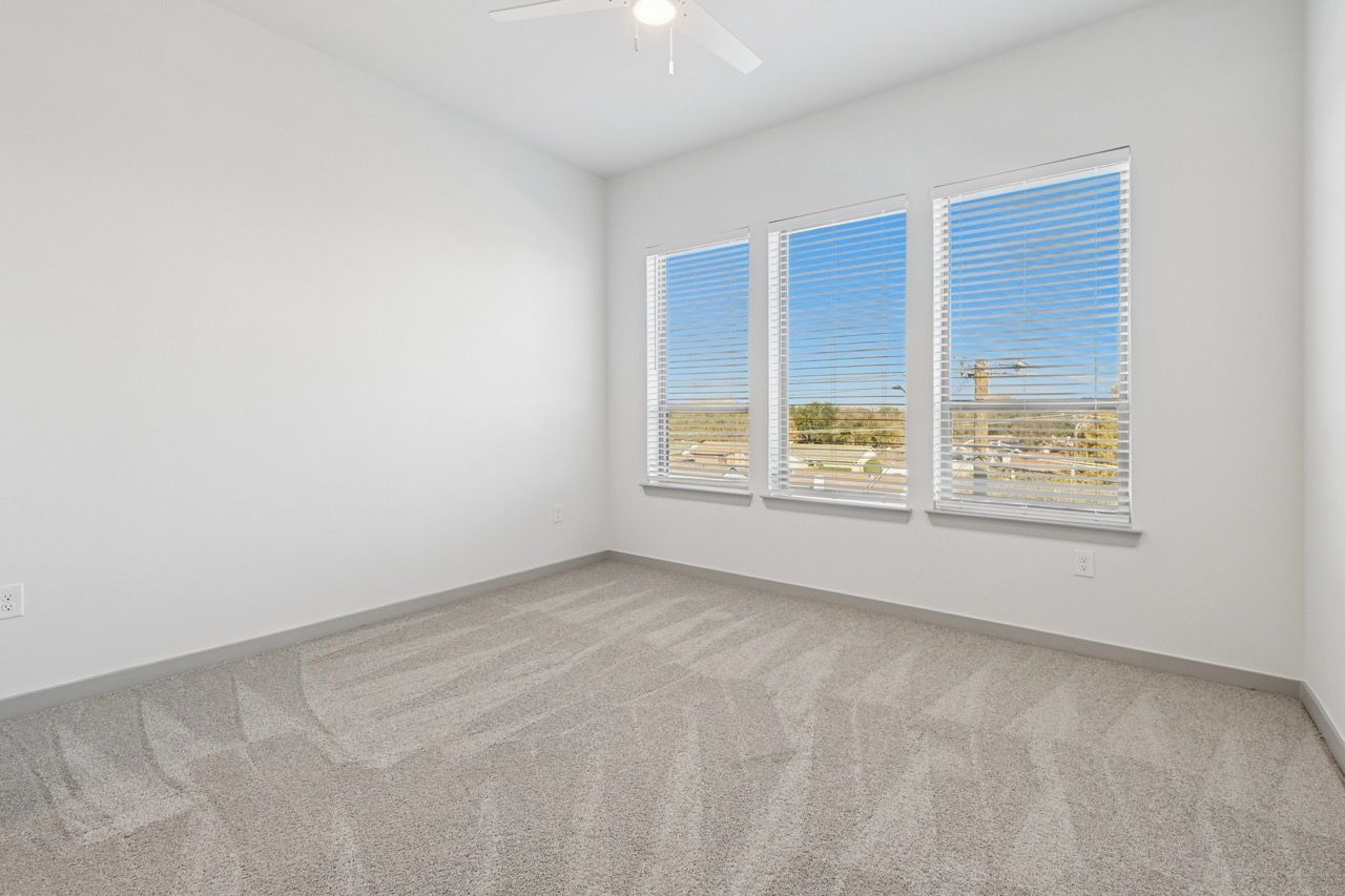 Empty carpeted bedroom with three windows and blinds  at Ennova Fulshear in Fulshear, TX.