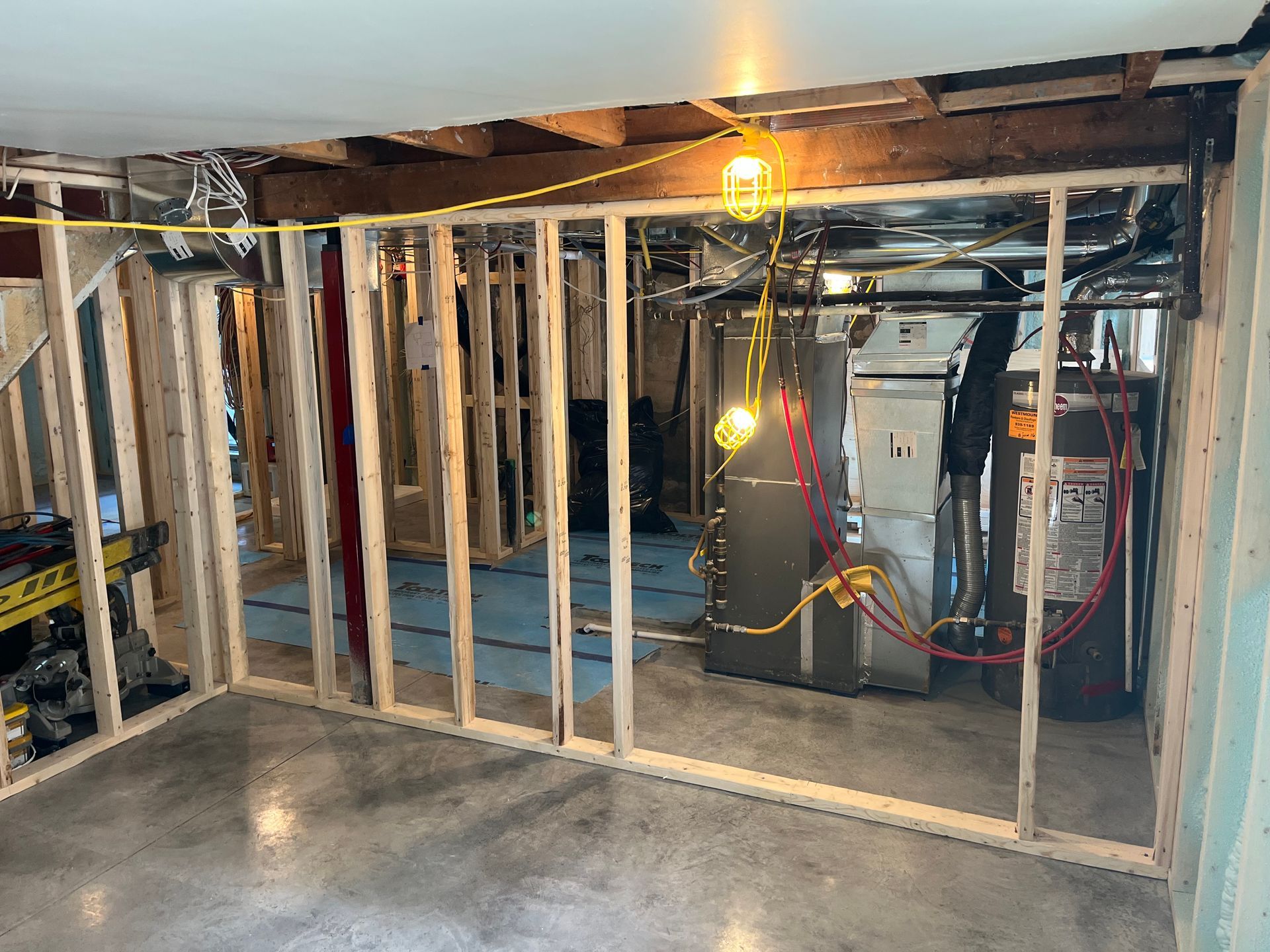 Sous-sol en construction, avec ossature bois autour d'un local technique. Câblage électrique apparent et sols en béton nu.