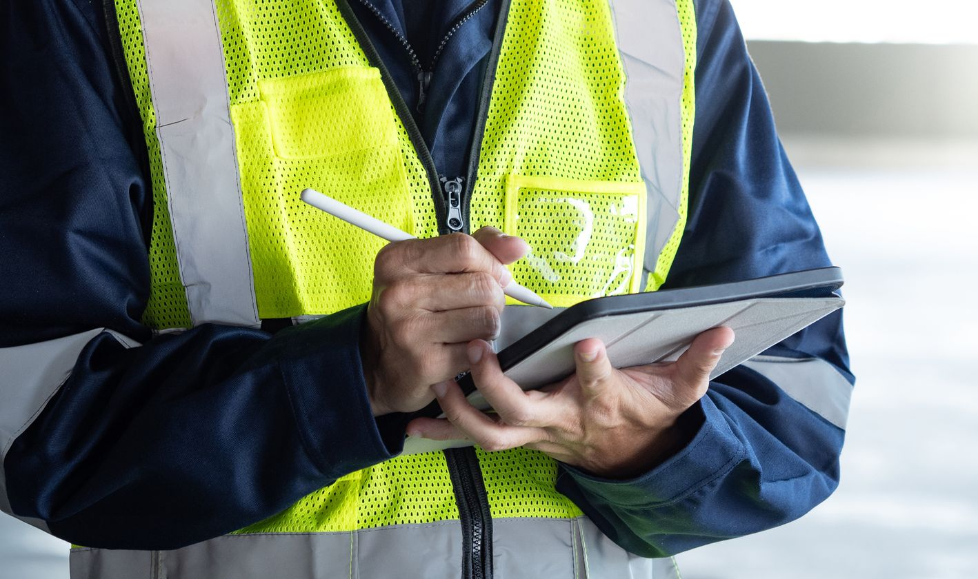 Famille dans un salon lumineux : père sur le canapé utilisant une tablette, mère avec deux enfants, salle à manger en arrière-plan.