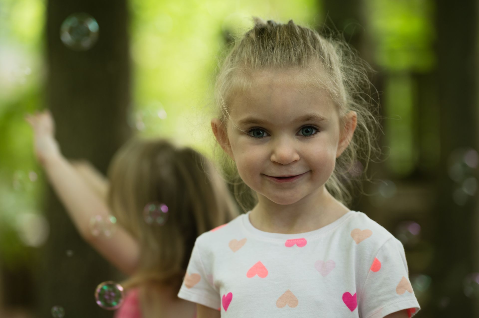 A little girl is standing in front of soap bubbles.