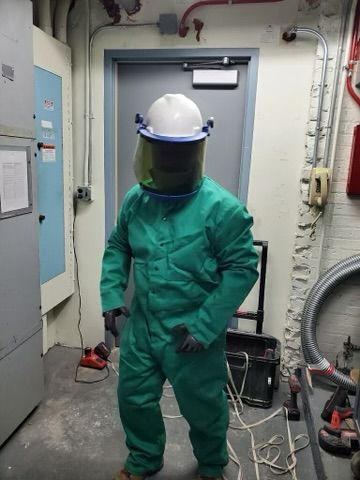 Person in green safety suit, hard hat, and face shield in an industrial setting.
