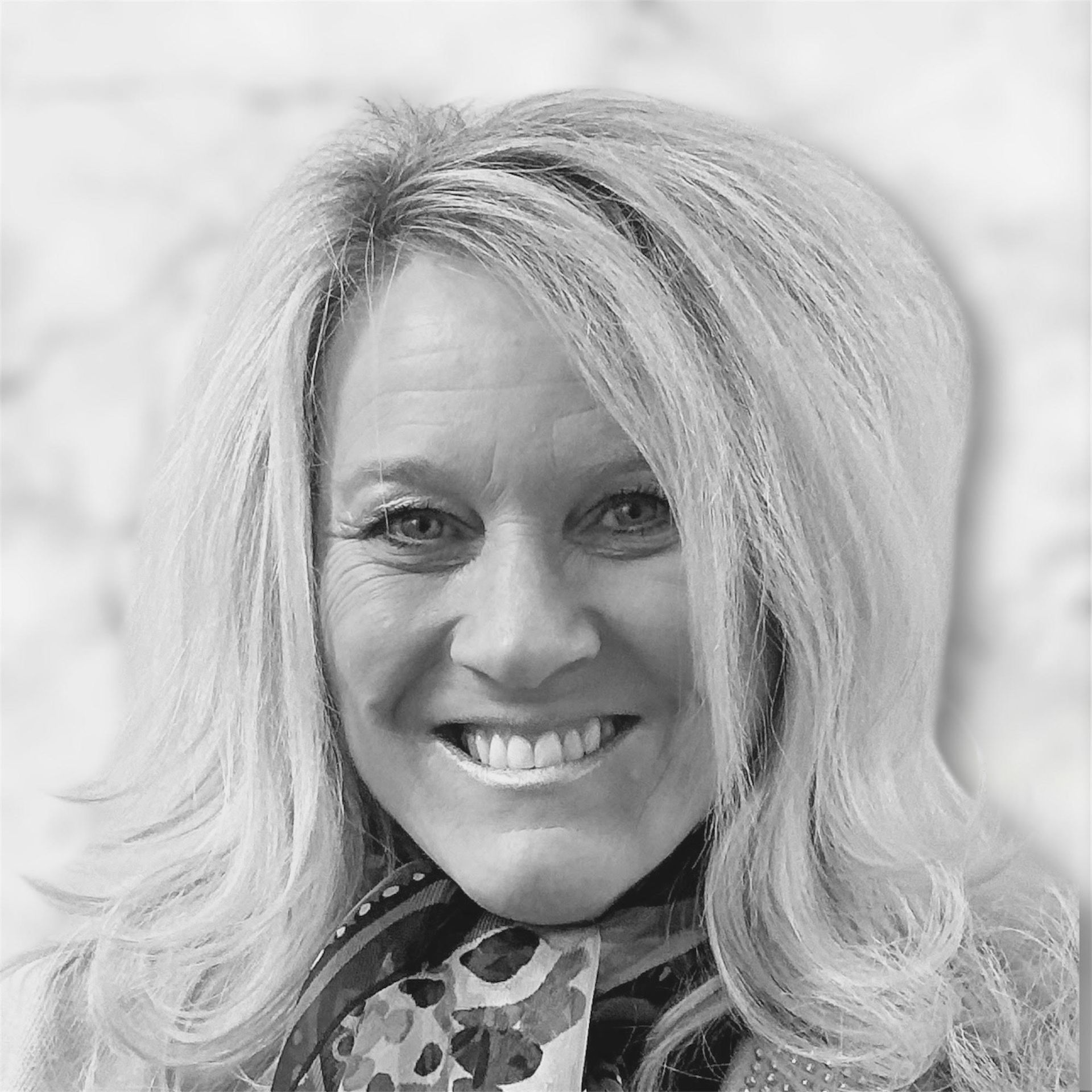 Woman with blonde hair smiles, wearing a scarf with a patterned design.