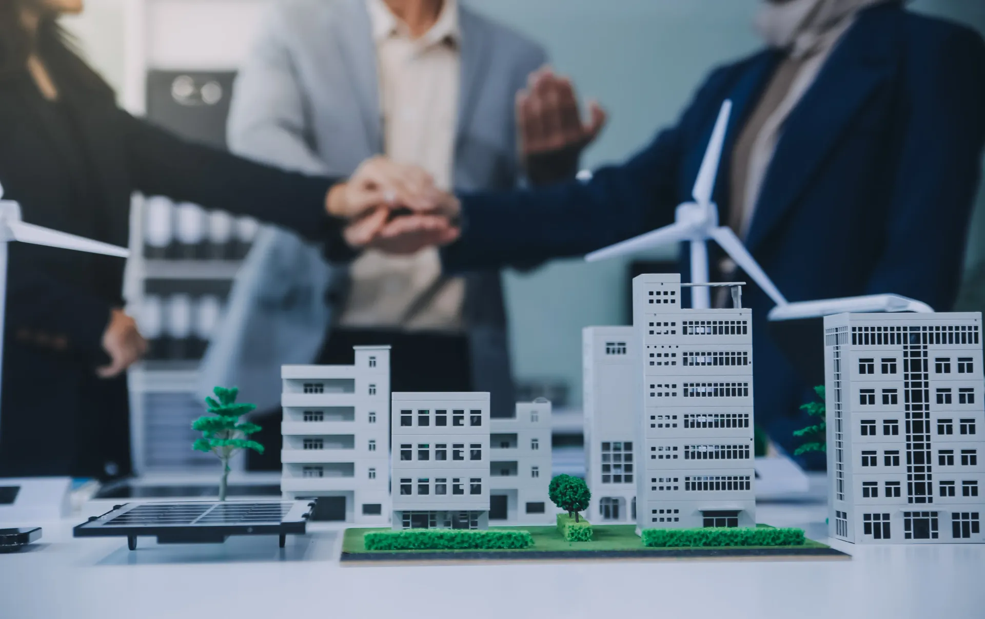 Business team huddling over a model city with wind turbines and solar panels, symbolizing sustainability.