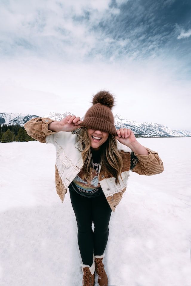 girl smiling in the snow while pulling her beanie