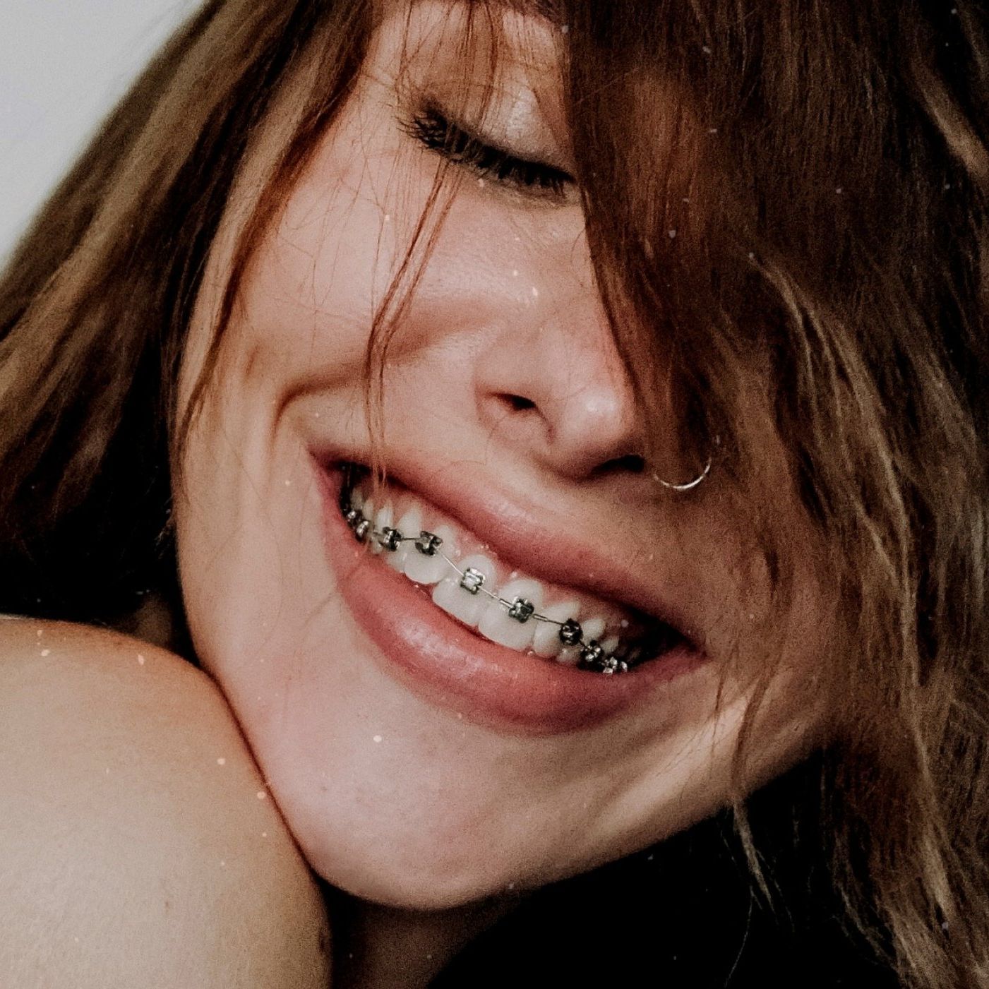 A woman with braces on her teeth is smiling with her eyes closed.